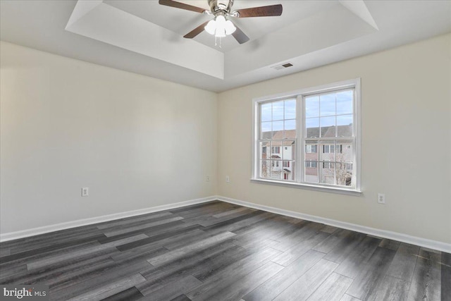 empty room featuring a tray ceiling, ceiling fan, and dark wood-type flooring