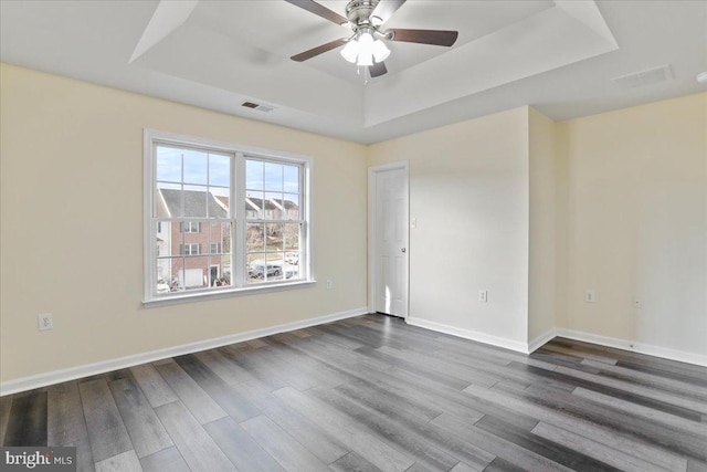 empty room with ceiling fan, a raised ceiling, and wood-type flooring