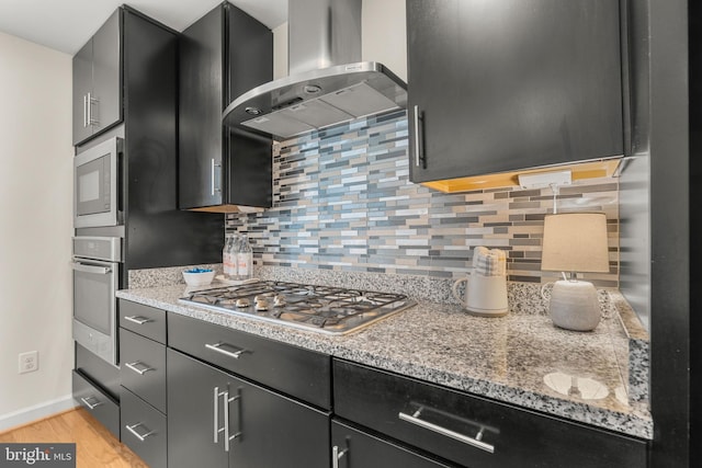 kitchen with backsplash, extractor fan, light wood-type flooring, light stone countertops, and appliances with stainless steel finishes