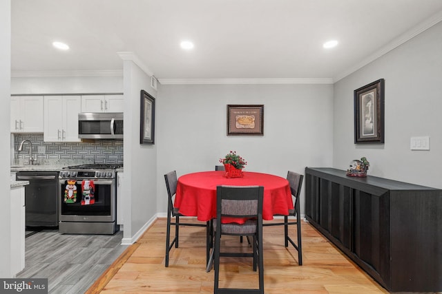 dining room with crown molding, sink, and light hardwood / wood-style floors