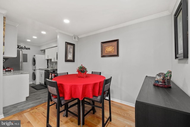 dining area featuring stacked washer / dryer, ornamental molding, and light wood-type flooring