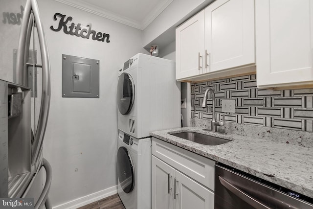 laundry area featuring sink, dark wood-type flooring, cabinets, stacked washer and dryer, and ornamental molding