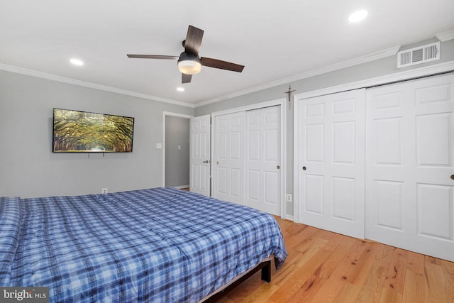 bedroom with ceiling fan, hardwood / wood-style floors, two closets, and ornamental molding