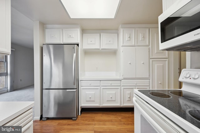 kitchen with light wood-style floors, white cabinets, light countertops, freestanding refrigerator, and white range with electric cooktop