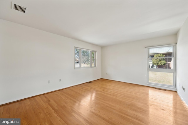 empty room featuring light wood-type flooring, a healthy amount of sunlight, and visible vents