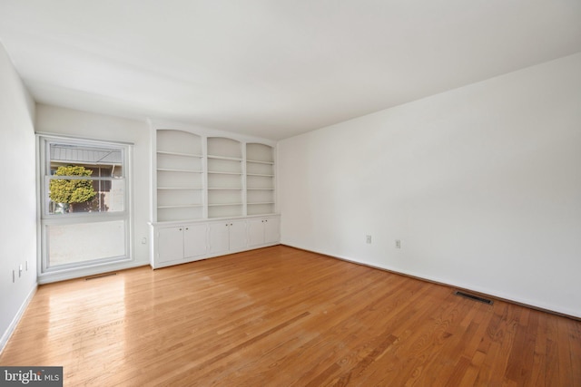 spare room with baseboards, built in shelves, visible vents, and light wood-style floors