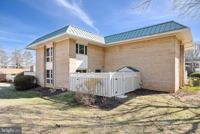 view of property exterior with metal roof, brick siding, a standing seam roof, and a lawn