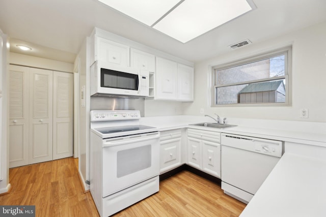 kitchen featuring white appliances, white cabinets, light countertops, light wood-type flooring, and a sink