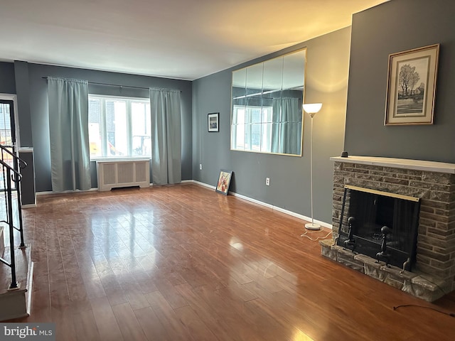 unfurnished living room featuring a fireplace, radiator heating unit, and wood-type flooring