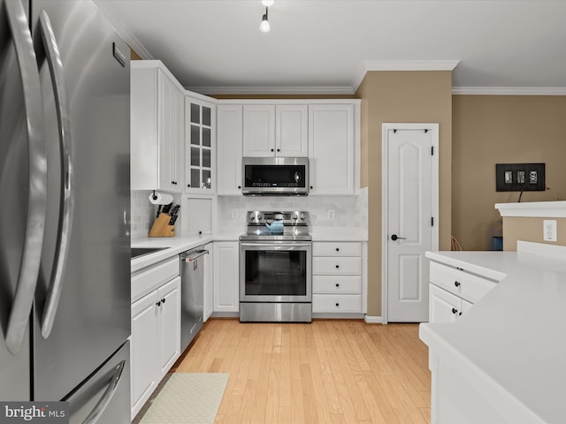 kitchen featuring stainless steel appliances, backsplash, light hardwood / wood-style floors, white cabinets, and ornamental molding