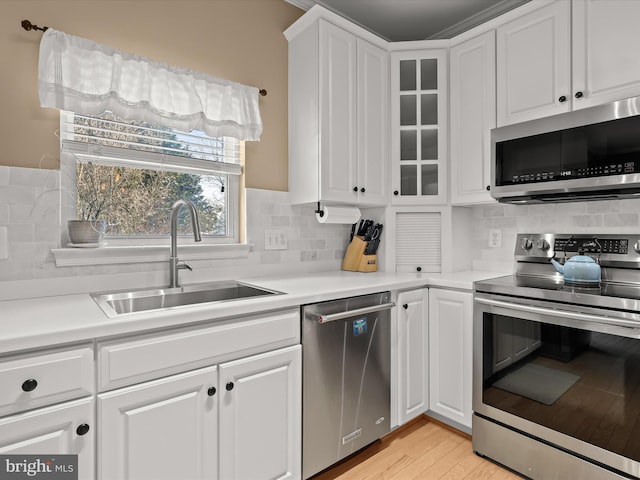 kitchen with sink, decorative backsplash, appliances with stainless steel finishes, light hardwood / wood-style floors, and white cabinetry