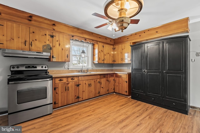 kitchen with light wood finished floors, stainless steel electric stove, light countertops, under cabinet range hood, and a sink