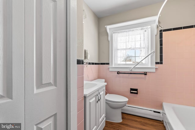 full bathroom with toilet, a baseboard heating unit, wood finished floors, tile walls, and a bath