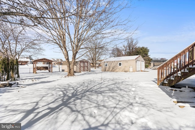 snowy yard with a garage, stairs, and an outdoor structure