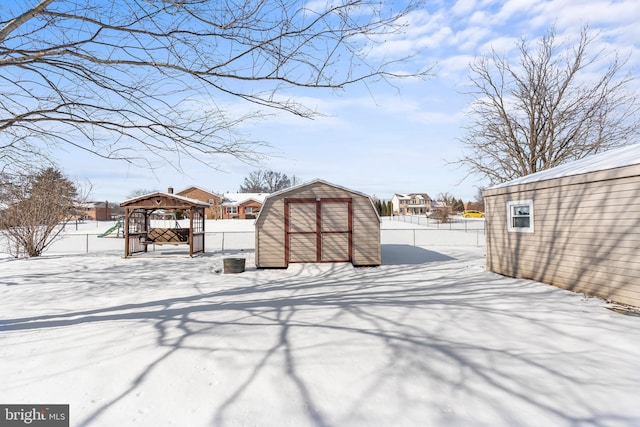 yard covered in snow with a fenced backyard, an outdoor structure, a gazebo, and a shed