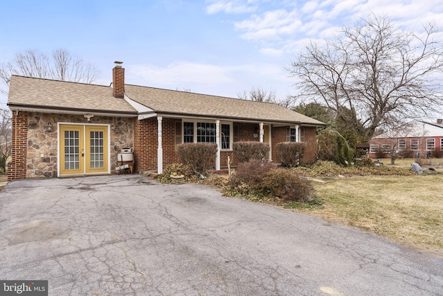 ranch-style house with french doors, roof with shingles, a chimney, stone siding, and driveway