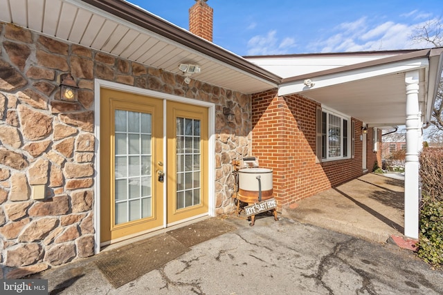 property entrance featuring stone siding, french doors, brick siding, and a chimney