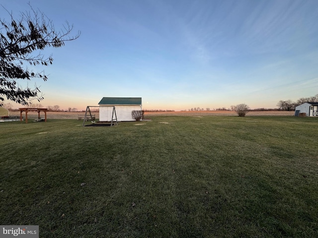 yard at dusk with a rural view and an outdoor structure