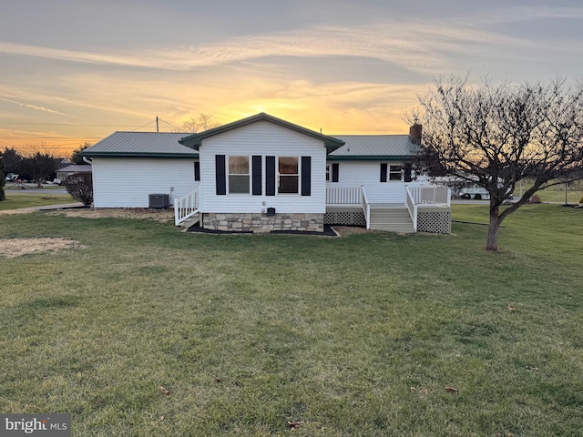 back house at dusk with central AC unit, a deck, and a lawn