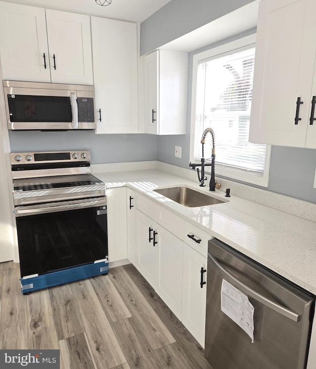 kitchen with sink, light hardwood / wood-style floors, light stone counters, white cabinetry, and stainless steel appliances