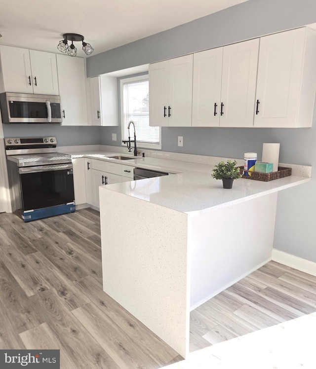 kitchen featuring kitchen peninsula, light wood-type flooring, stainless steel appliances, sink, and white cabinetry