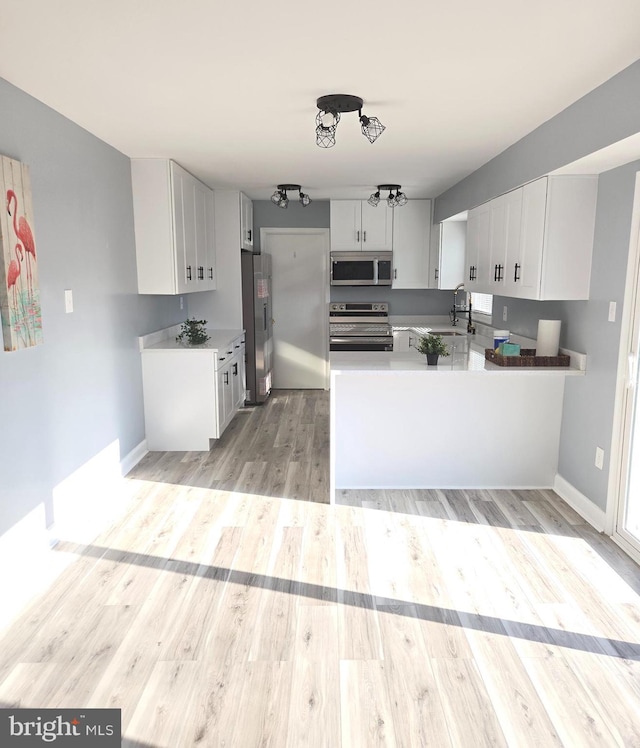 kitchen featuring kitchen peninsula, light wood-type flooring, stainless steel appliances, sink, and white cabinetry