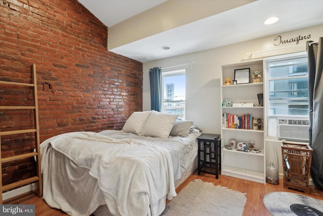 bedroom with lofted ceiling, wood-type flooring, and brick wall