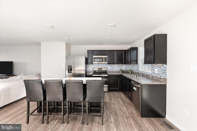 kitchen featuring sink, a breakfast bar, appliances with stainless steel finishes, light hardwood / wood-style floors, and a kitchen island