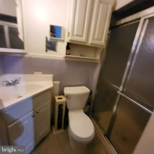 bathroom featuring vanity, tile patterned floors, toilet, tile walls, and a shower with shower door