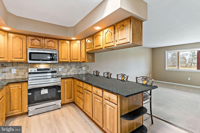 kitchen with light wood-type flooring, appliances with stainless steel finishes, backsplash, and dark stone countertops