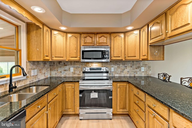 kitchen with decorative backsplash, appliances with stainless steel finishes, sink, light hardwood / wood-style flooring, and dark stone countertops