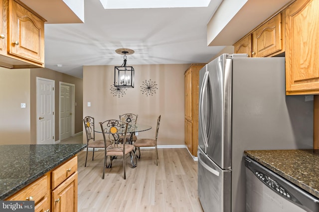 kitchen featuring stainless steel appliances, dark stone counters, a chandelier, decorative light fixtures, and light hardwood / wood-style floors