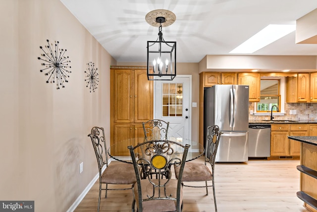 dining area with a skylight, sink, an inviting chandelier, and light hardwood / wood-style flooring