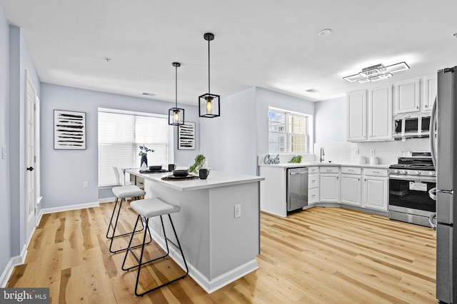 kitchen with white cabinetry, sink, light hardwood / wood-style floors, decorative light fixtures, and appliances with stainless steel finishes