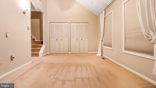 unfurnished bedroom featuring high vaulted ceiling, light colored carpet, and two closets