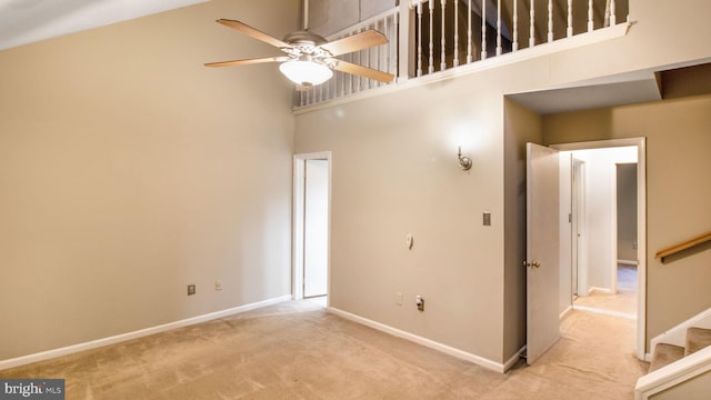 unfurnished room featuring ceiling fan, light colored carpet, and a high ceiling