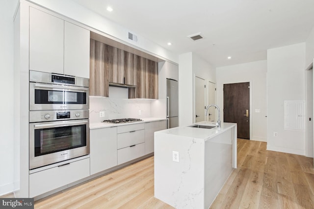 kitchen with white cabinetry, sink, light hardwood / wood-style flooring, an island with sink, and appliances with stainless steel finishes