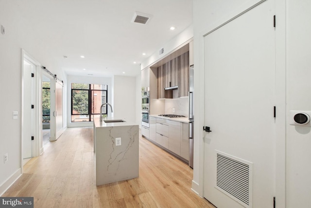 kitchen featuring a barn door, light hardwood / wood-style floors, a kitchen island with sink, and sink