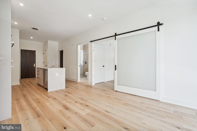 unfurnished room with a barn door, light hardwood / wood-style floors, and sink