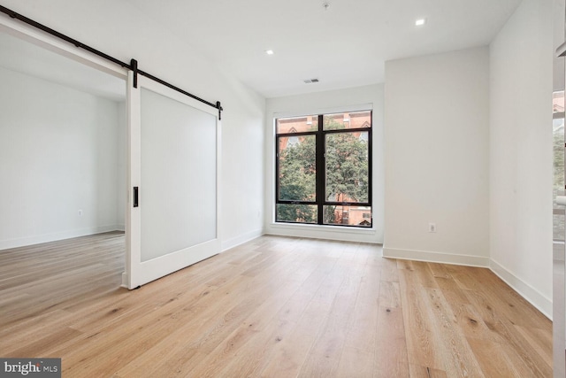 unfurnished bedroom with a barn door and light hardwood / wood-style flooring