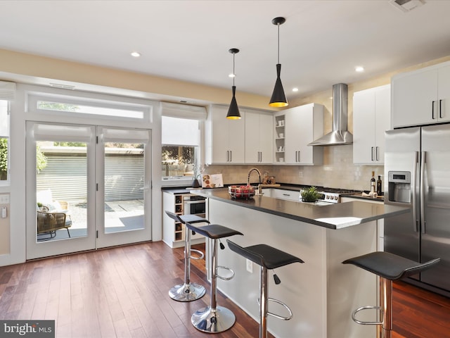 kitchen featuring wall chimney range hood, white cabinets, a kitchen bar, and stainless steel refrigerator with ice dispenser