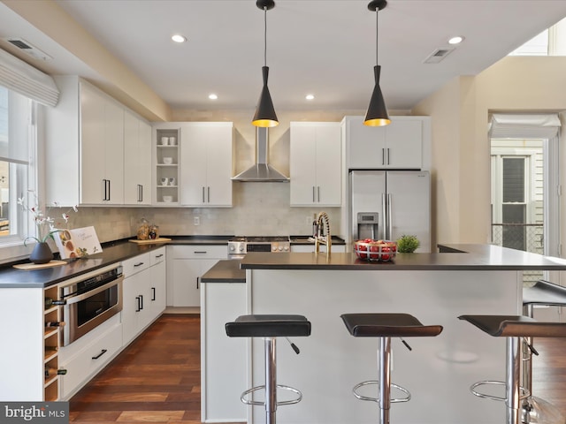 kitchen with a breakfast bar, wall chimney exhaust hood, appliances with stainless steel finishes, tasteful backsplash, and white cabinetry