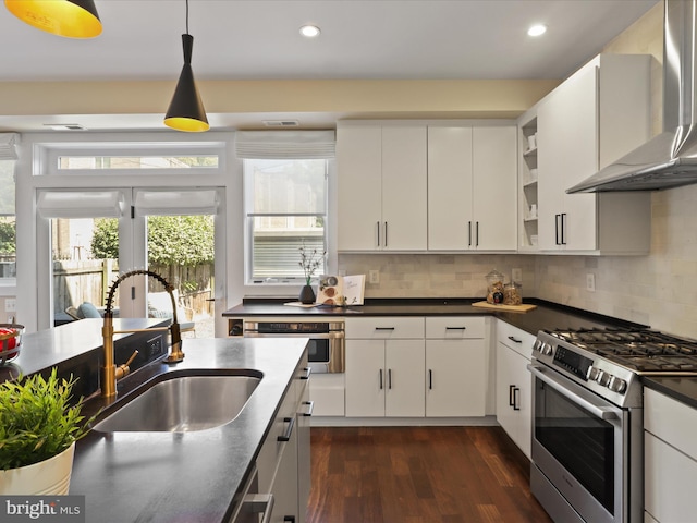 kitchen with wall chimney range hood, sink, decorative backsplash, appliances with stainless steel finishes, and white cabinetry