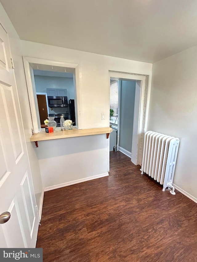 interior space featuring radiator, a kitchen breakfast bar, dark hardwood / wood-style floors, kitchen peninsula, and stainless steel appliances