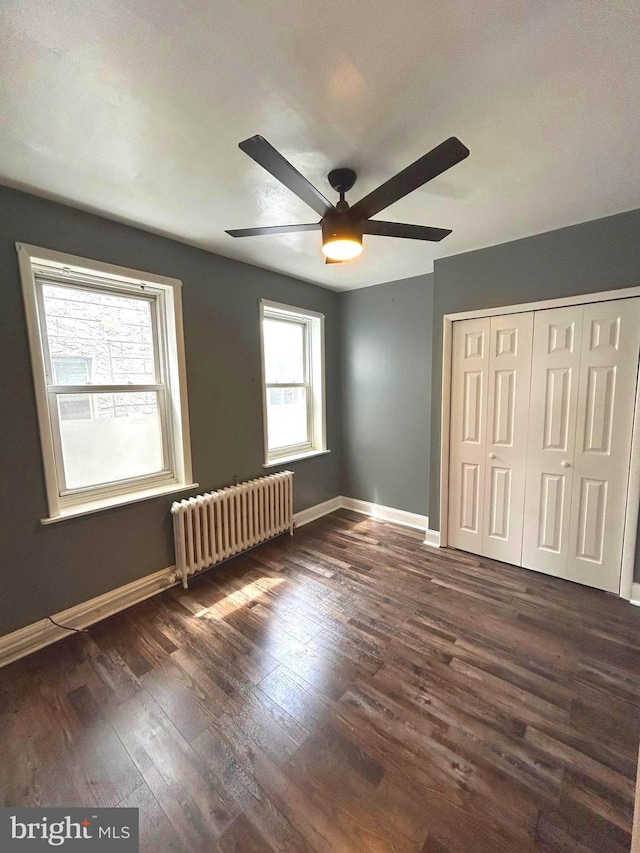 unfurnished bedroom featuring radiator, ceiling fan, a closet, and dark wood-type flooring