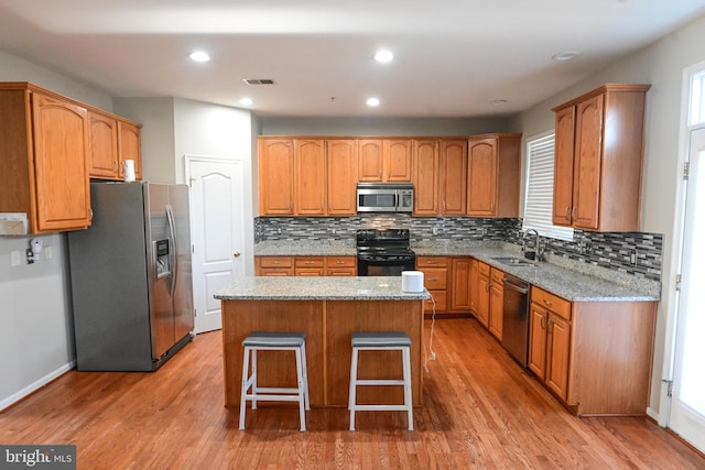 kitchen featuring light stone countertops, a center island, hardwood / wood-style floors, a breakfast bar, and appliances with stainless steel finishes