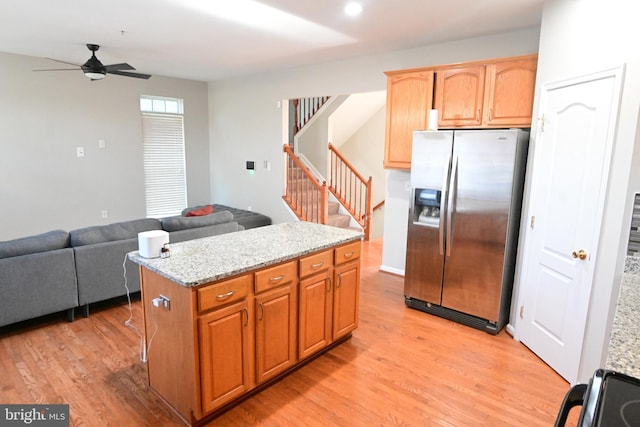 kitchen featuring a center island, stainless steel refrigerator with ice dispenser, ceiling fan, light wood-type flooring, and light stone counters