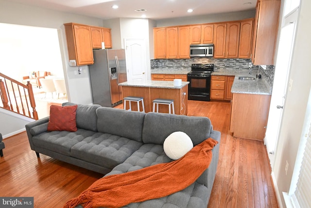 kitchen with sink, light stone counters, light hardwood / wood-style floors, a kitchen island, and appliances with stainless steel finishes