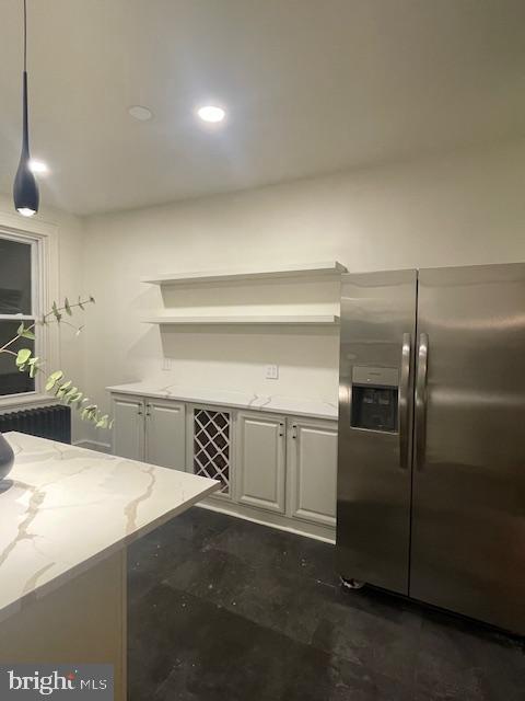 kitchen with stainless steel fridge, white cabinetry, and light stone countertops