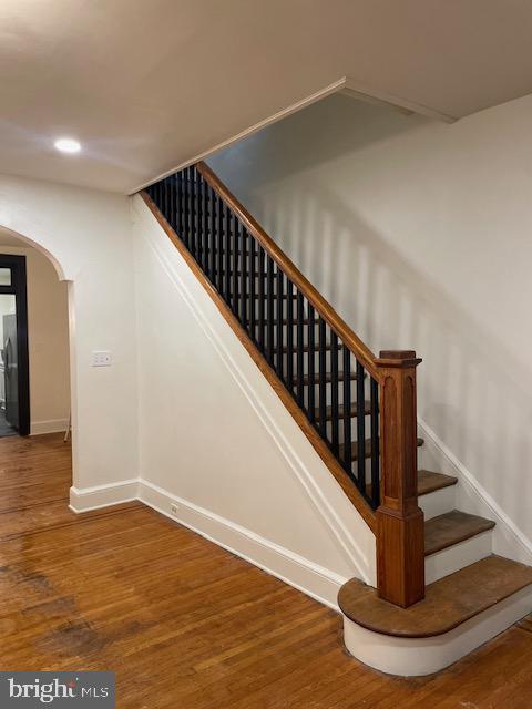 staircase featuring recessed lighting, baseboards, arched walkways, and wood finished floors